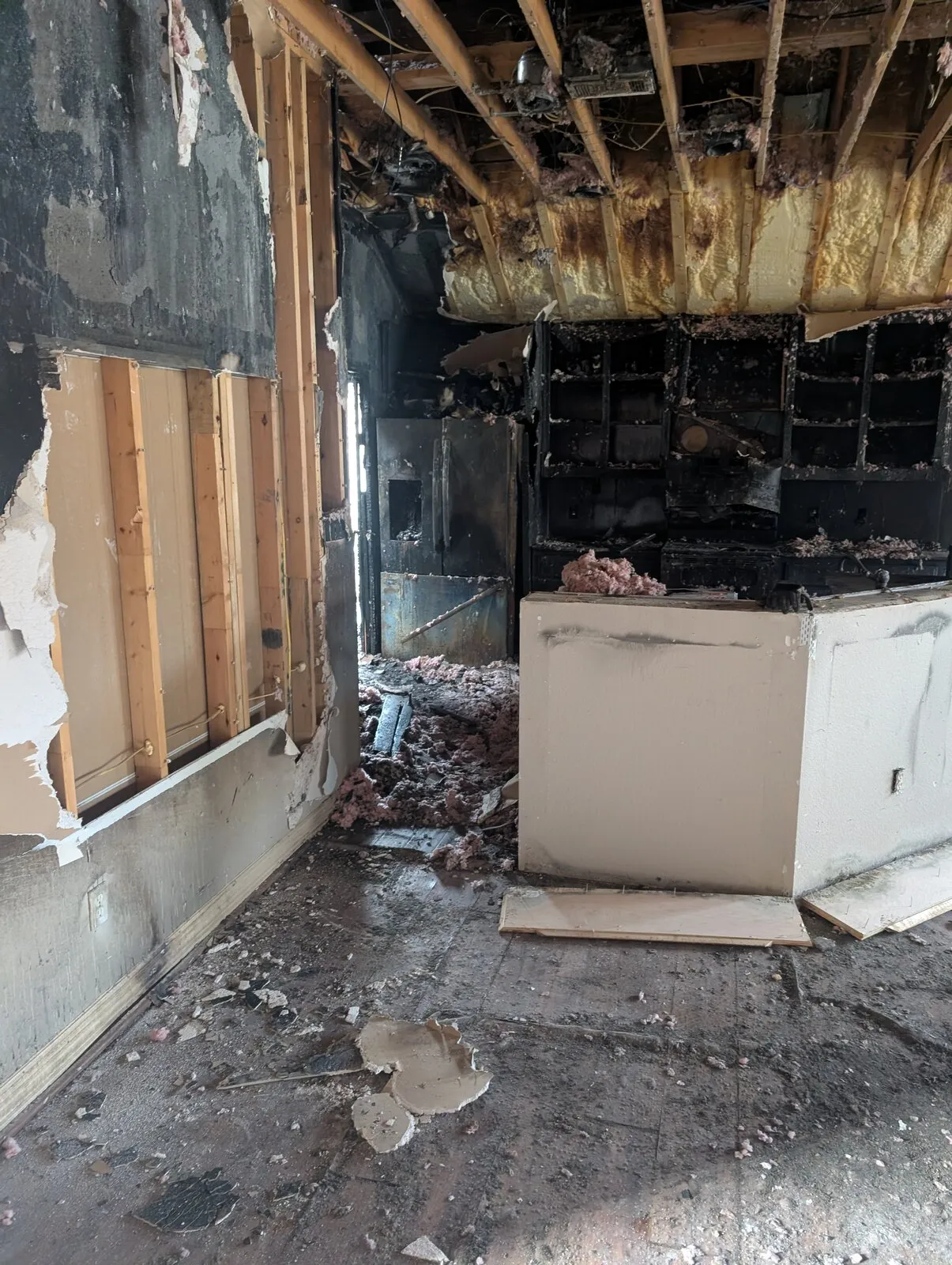 A room with the wall burned back to the studs and debris across the floor.