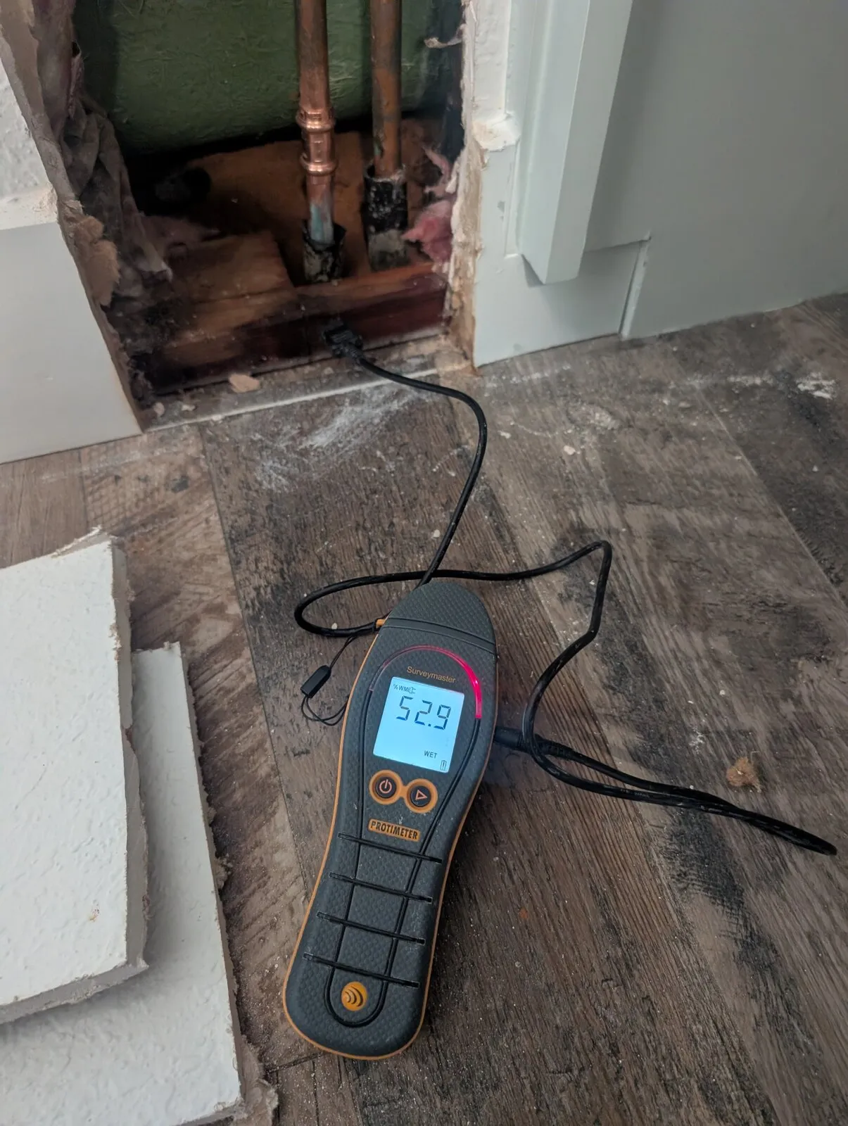 A moisture meter on the floor in front of an opened wall cavity.