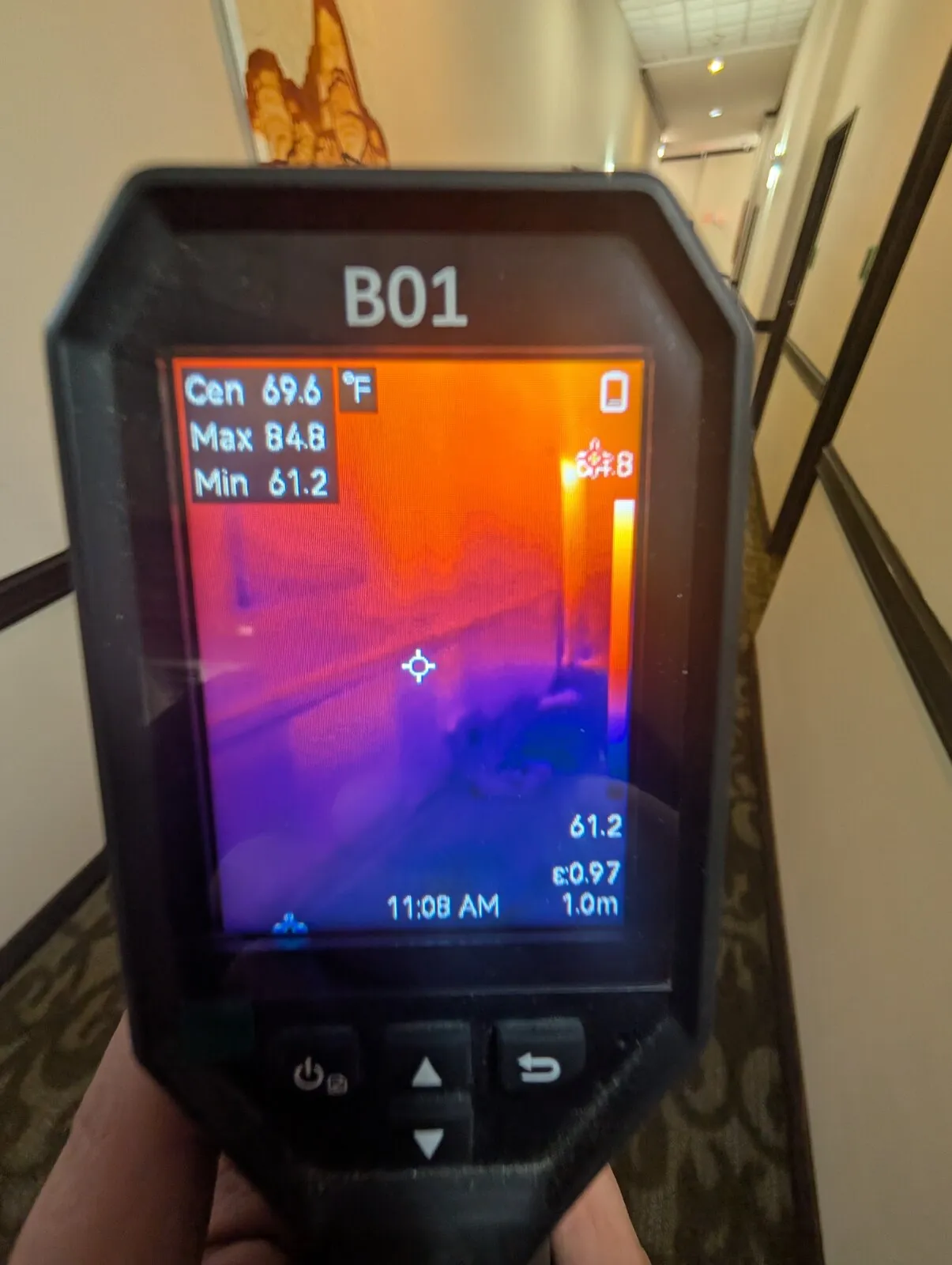 A technician holding a thermal camera up to a wall, the screen showing a cool patch.