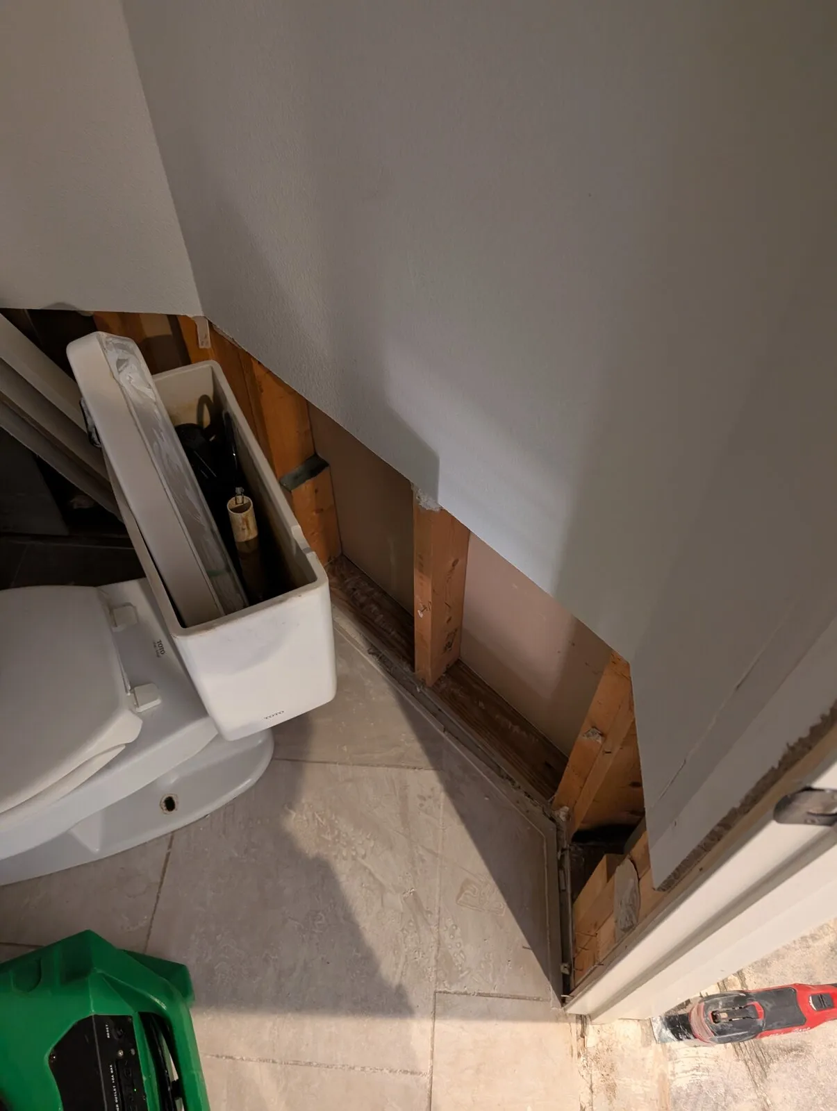 Drywall cut away beside a bathroom vanity, exposing the framing behind it.